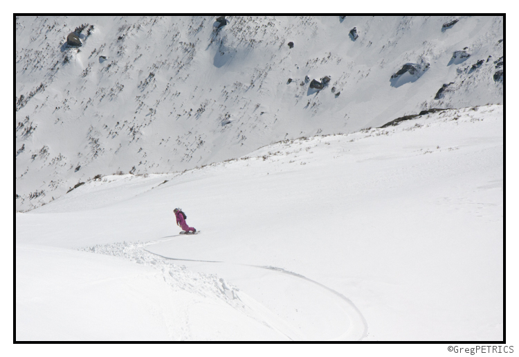 a view into the valley over a snowboarder riding pow